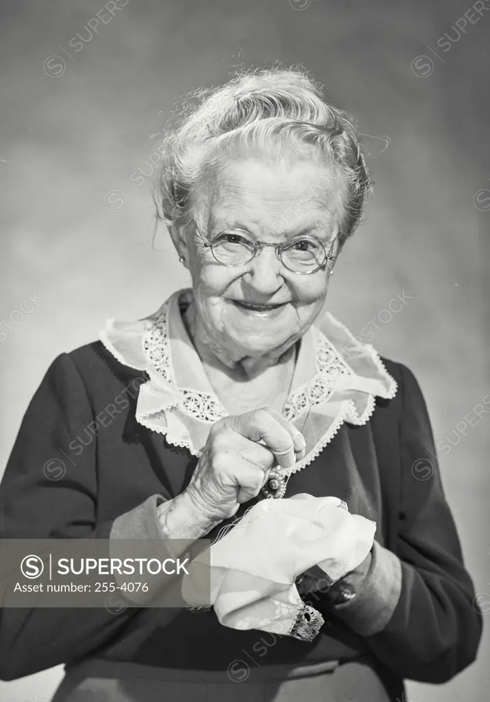 Vintage Photograph. Elderly woman holding up handkerchief she's sewing with thread and needle