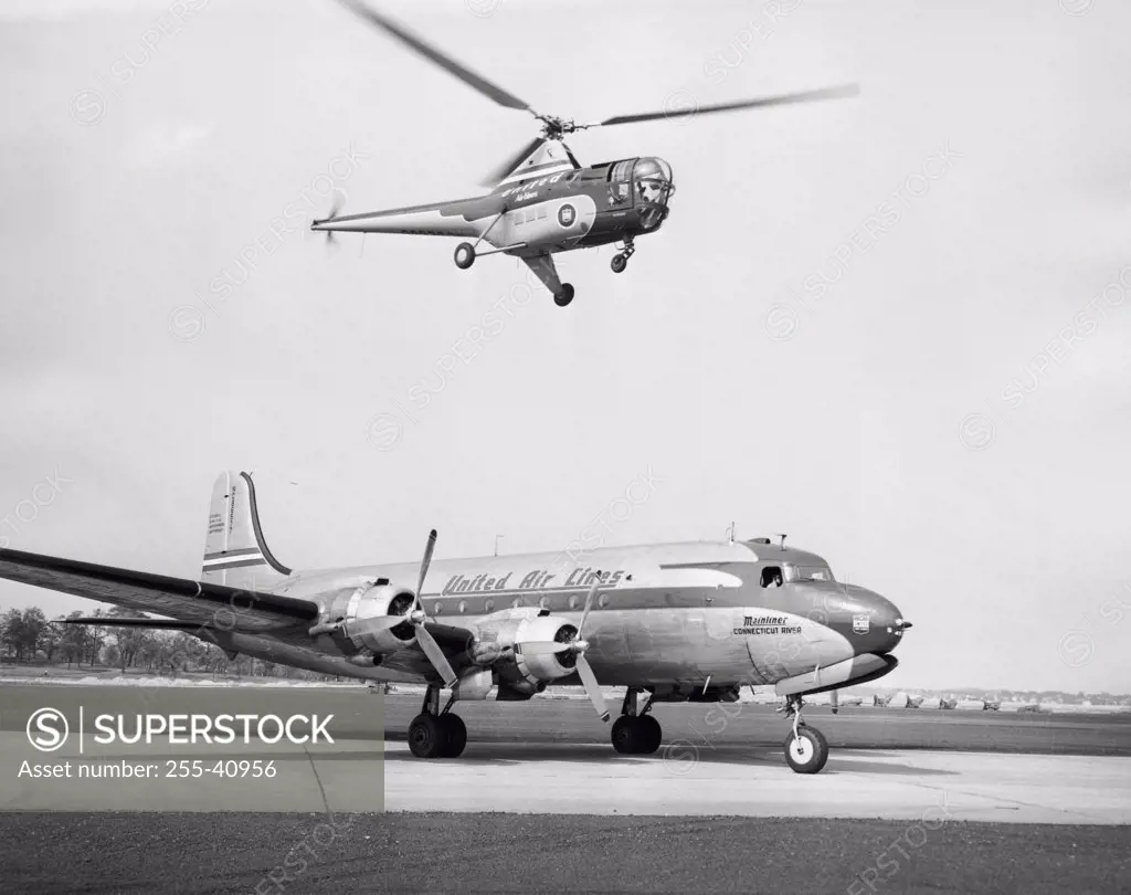 Low angle view of a helicopter in flight and an airplane at an airport, Sikorsky Helicopter, Douglas DC-4