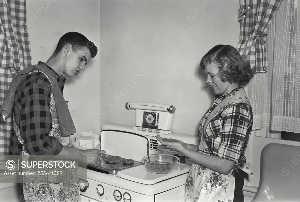 Vintage Photograph. Teenage couple making hamburgers on grill atop kitchen stove.