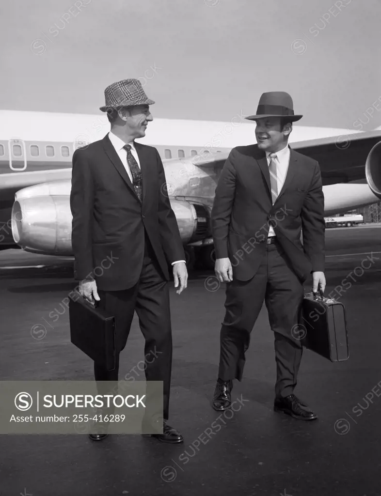 Two men walking along airplane at airport