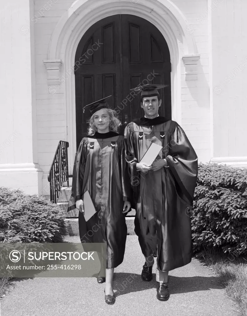 Female and male students wearing graduation gown holding diploma