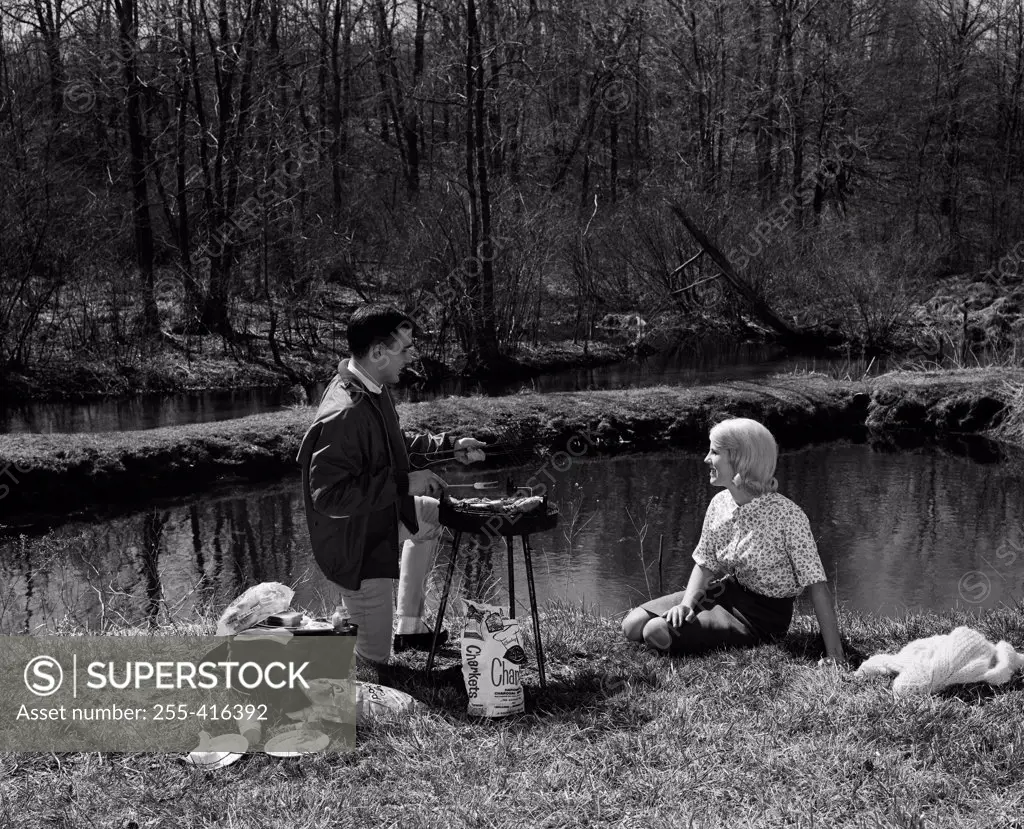 Young couple grilling on river bank