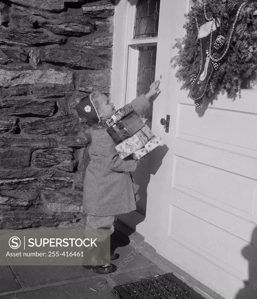 Girl carrying Christmas gifts and ringing door bell