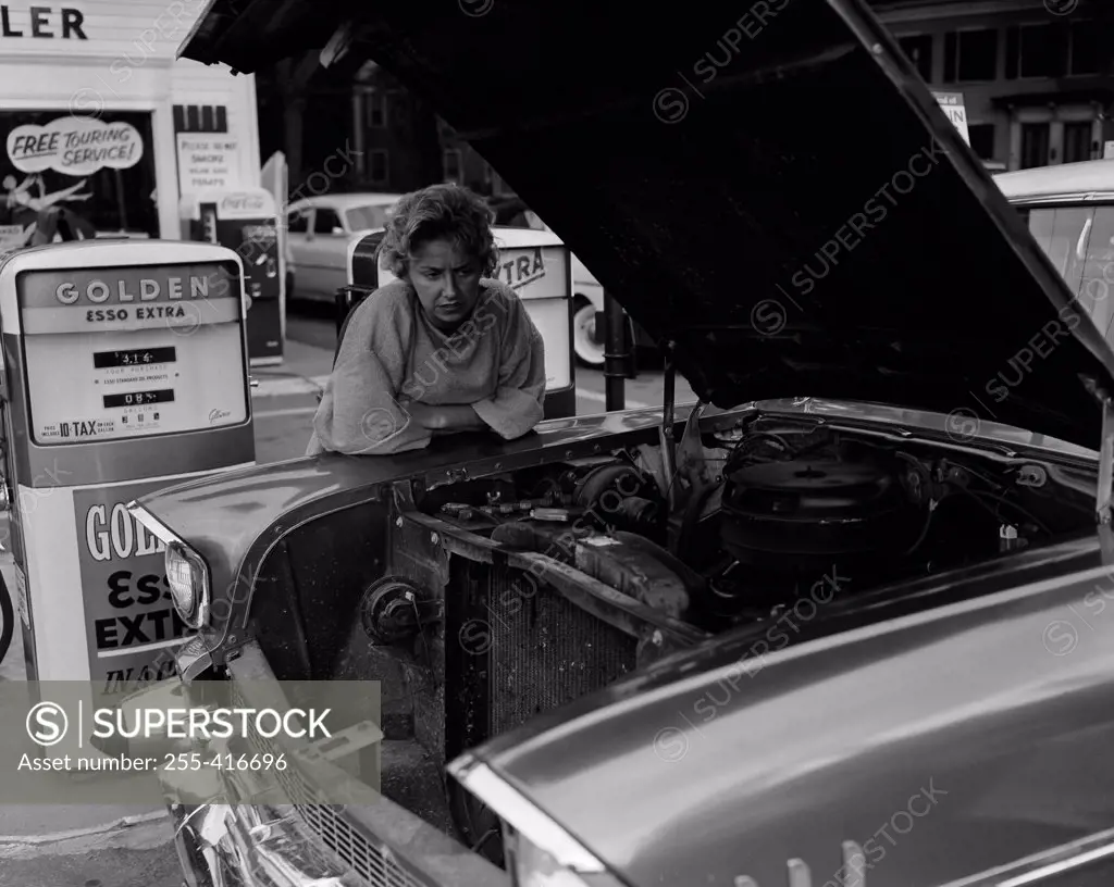 Mature woman leaning against car and looking  at car engine