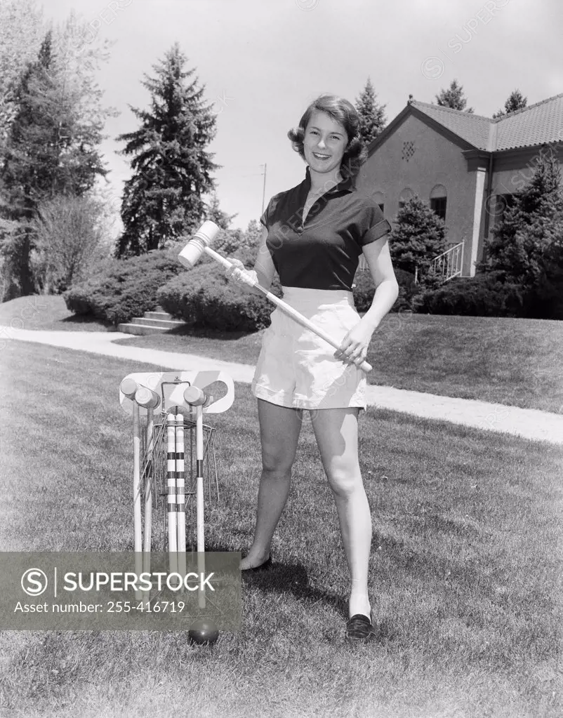 Young woman standing on lawn holding croquet mallet