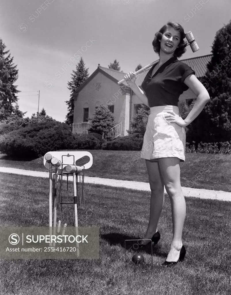 Young woman standing on lawn holding croquet mallet