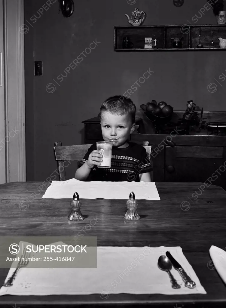 Boy sitting behind table drinking milk