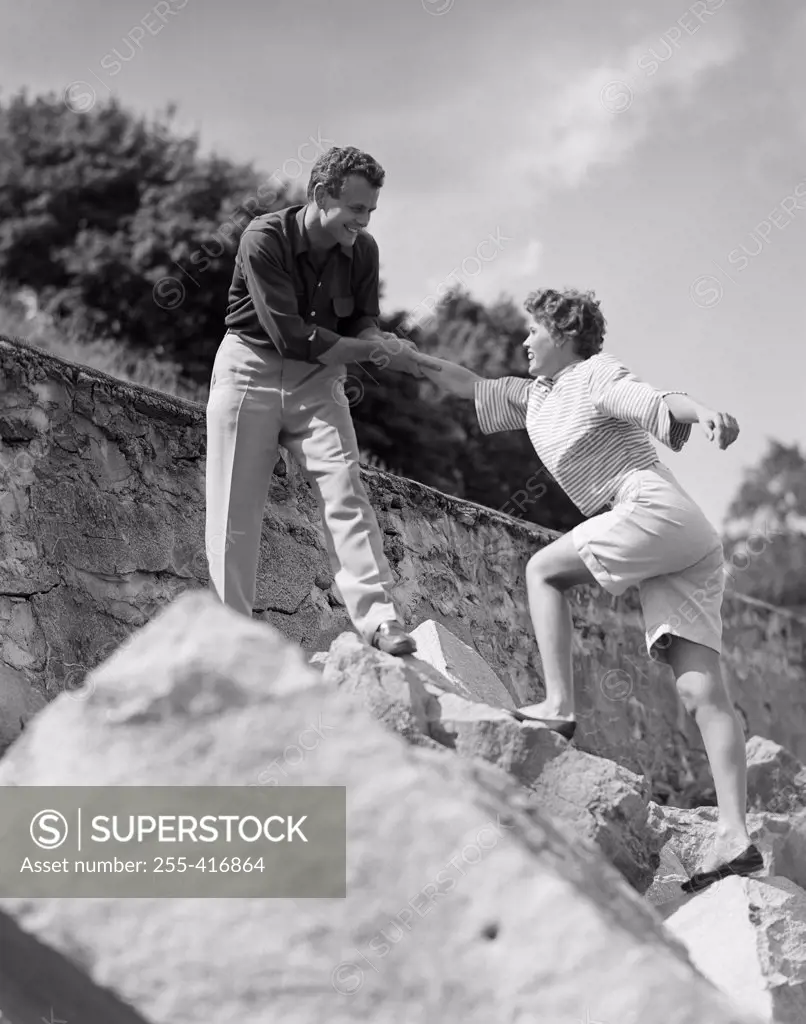Man assisting woman climbing on rock