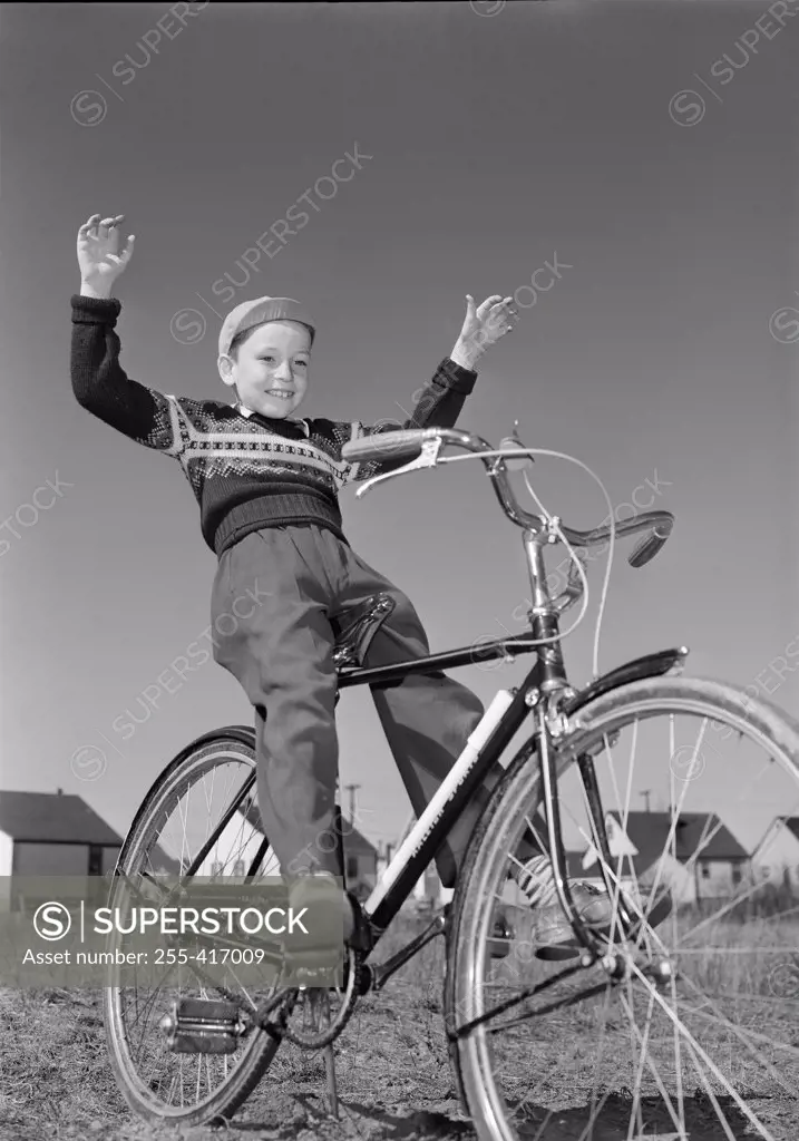 Boy riding bicycle with arms raised