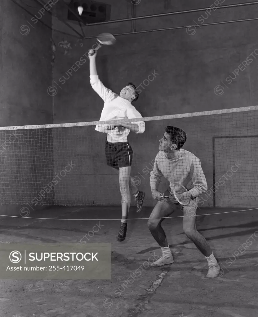 Two young men playing badminton in sports hall