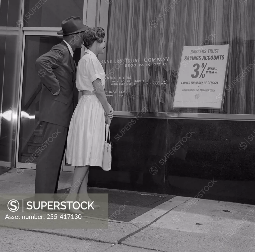 Mid adult couple examining bank offer, standing outside bank