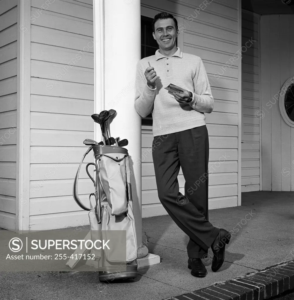 Mid adult man leaning against column with golf trolley beside