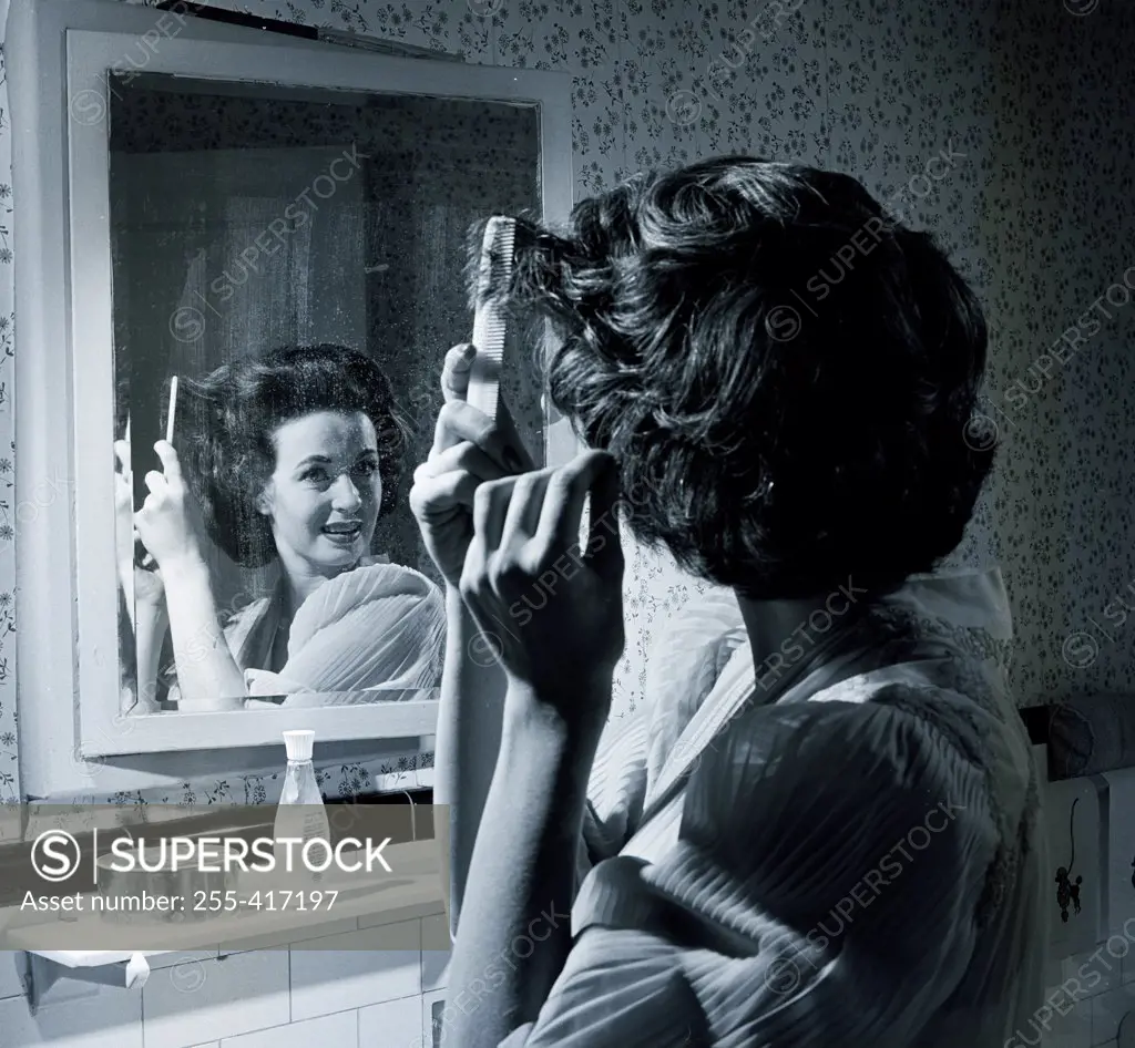 Woman combing hair in front of mirror