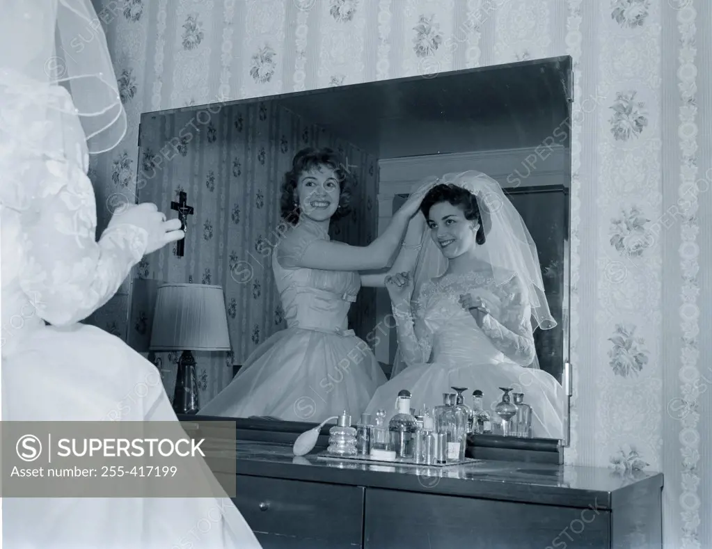 Bridesmaid attaching veil to bride's hair in front of mirror