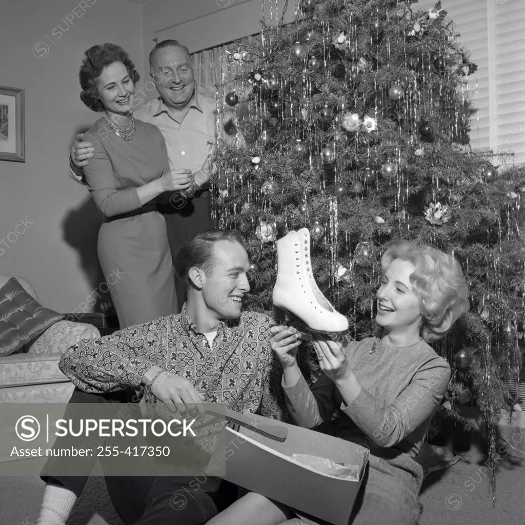 Young woman holding new ice skate, parents standing near Christmas tree