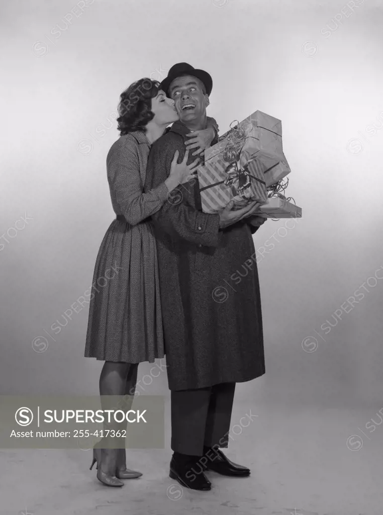 Woman kissing laughing man holding gifts, studio shot