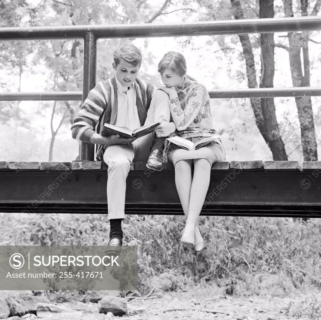 Teenage couple sitting on footbridge, doing homework
