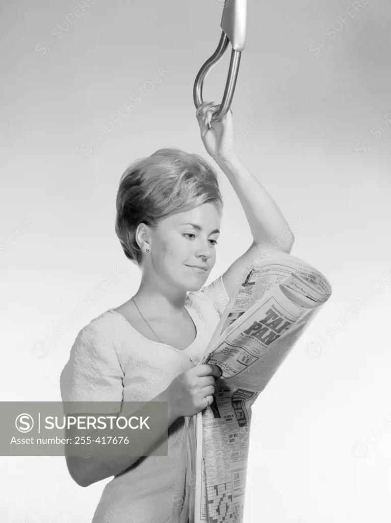 Young woman reading newspaper while holding handle