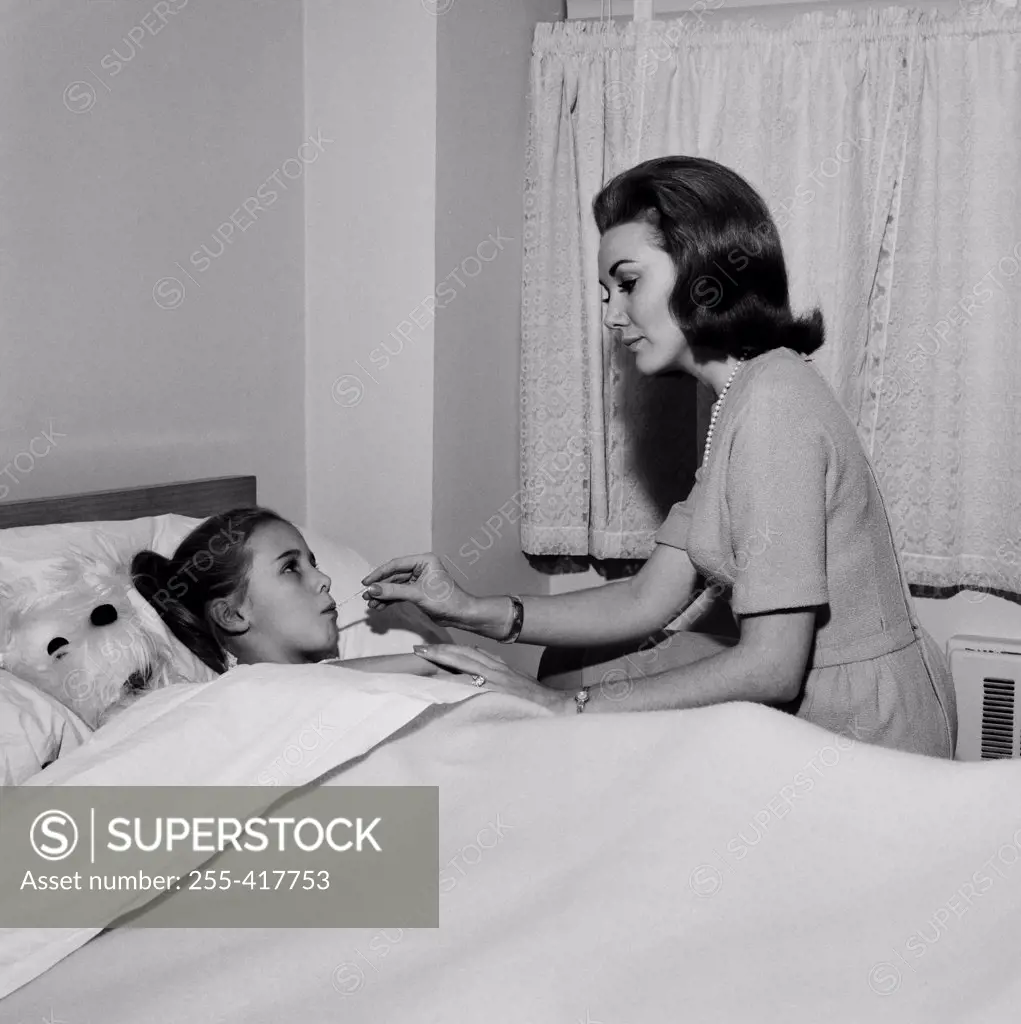 Mother checking daughter's temperature in bed