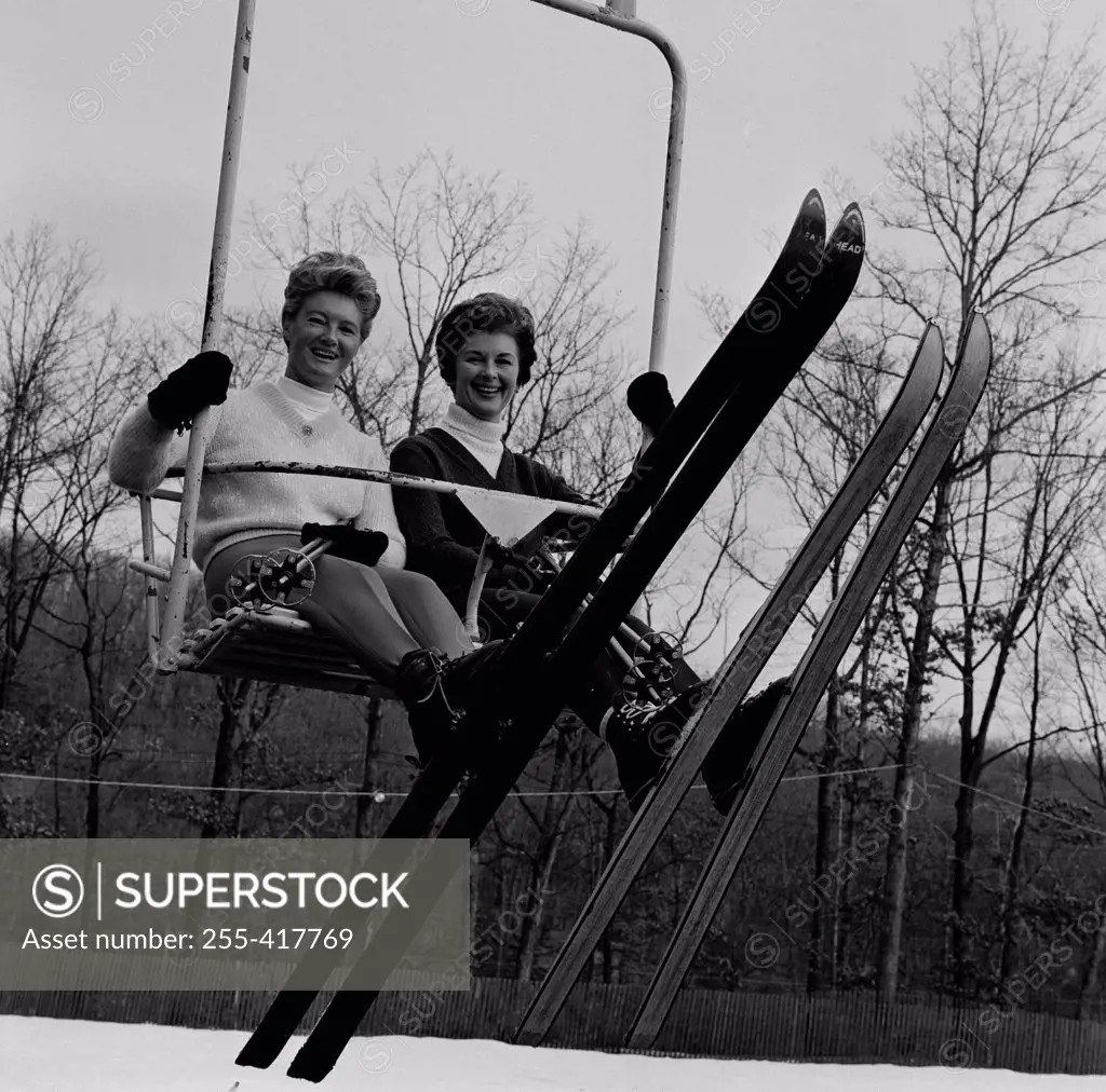 Two woman sitting ski lift, looking at camera and smiling