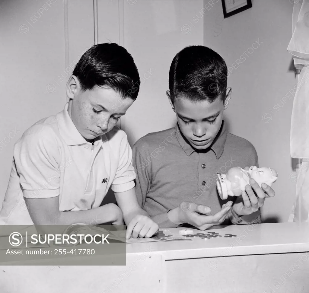 Two boys reading magazine and taking out money from money-box