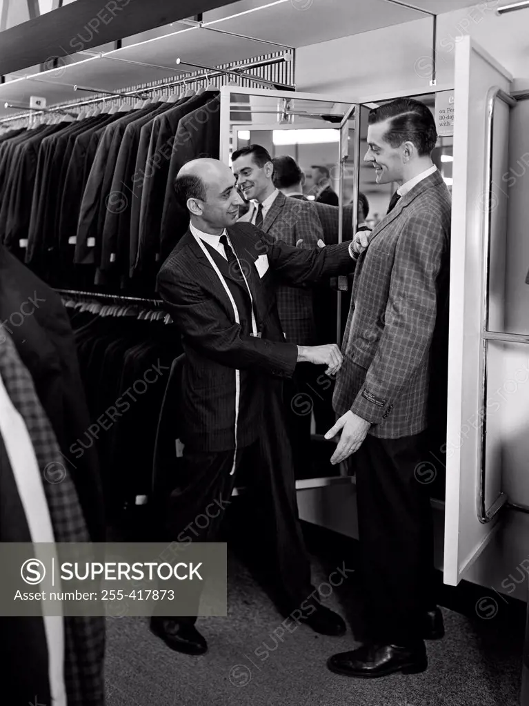 Shop assistant serving man trying on suit in shop