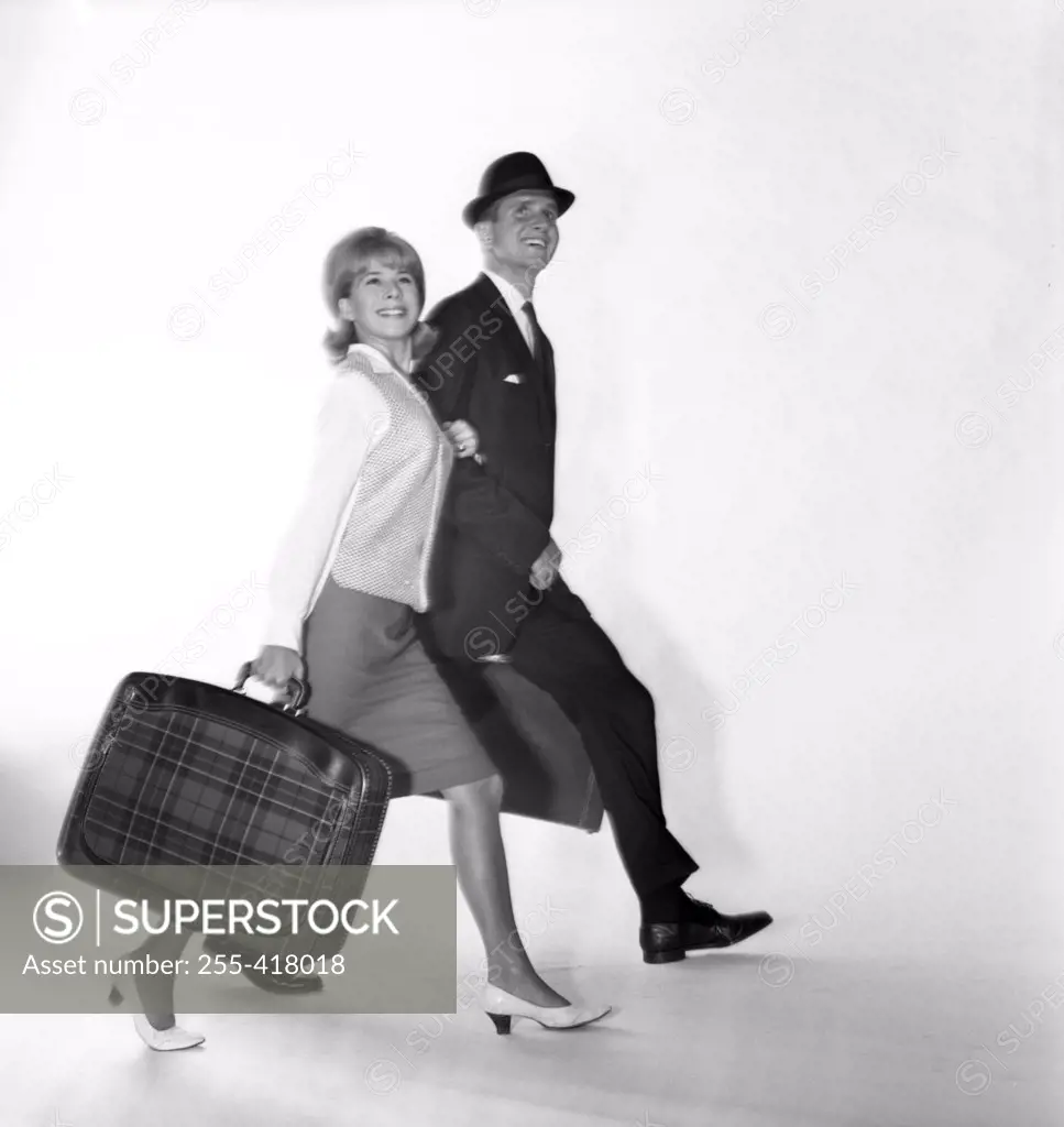 Mid adult couple carrying suitcases and smiling