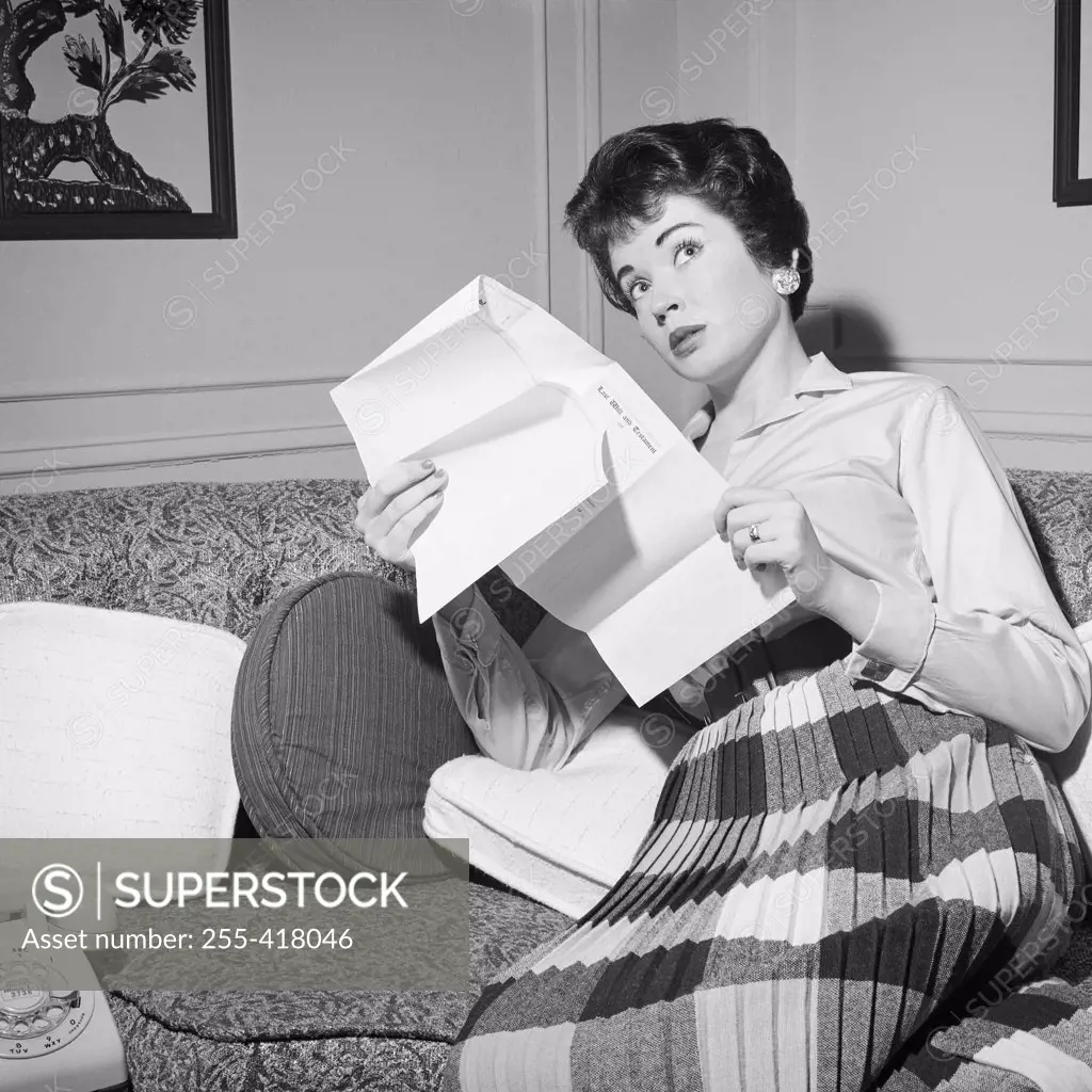Mid adult woman sitting on sofa holding letter