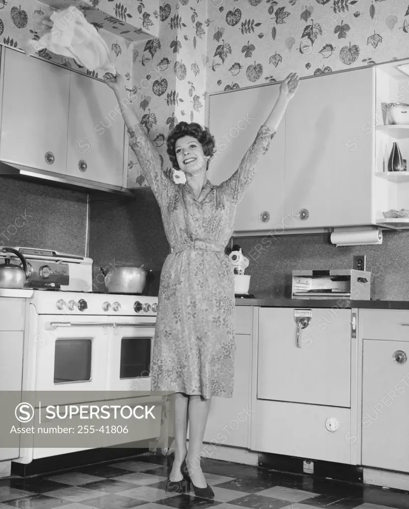 Young woman standing in a kitchen with her arms raised