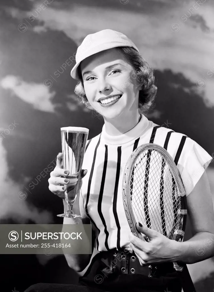 Portrait of smiling woman holding champagne and tennis racket