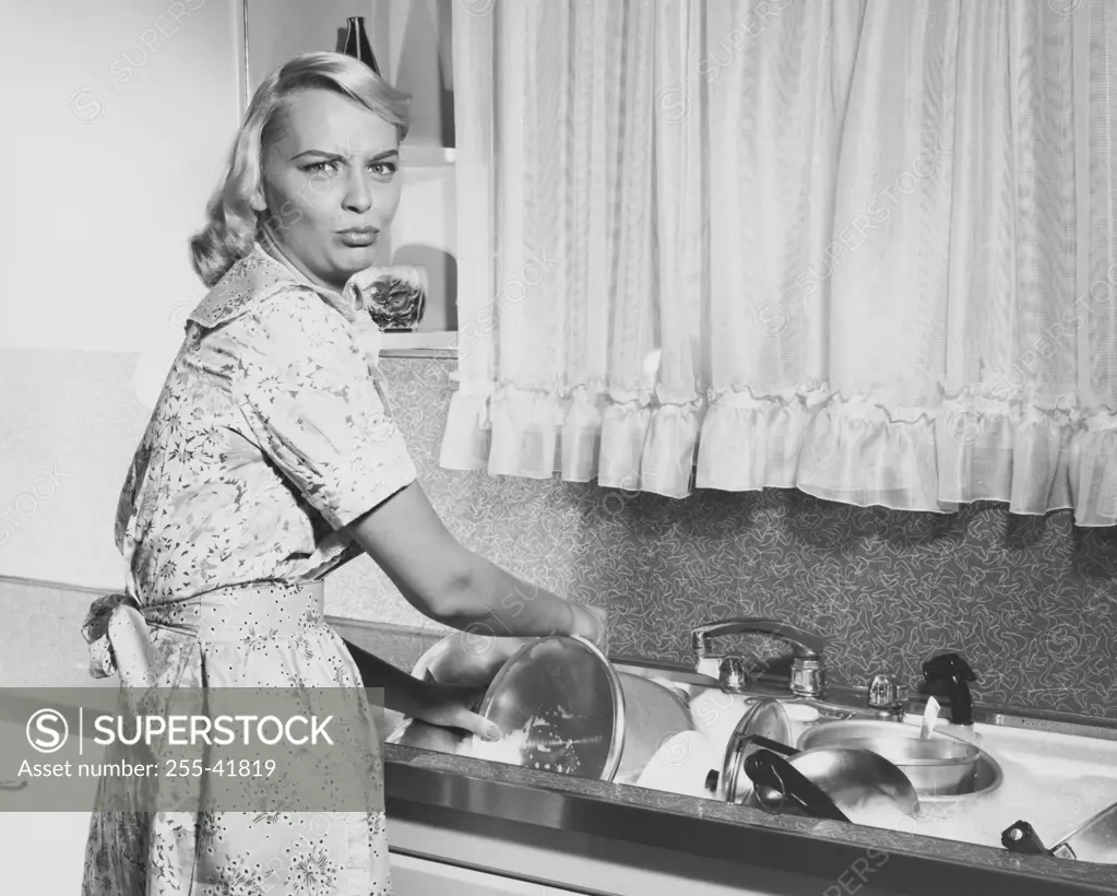 Portrait of a young woman washing pots and pans in a kitchen