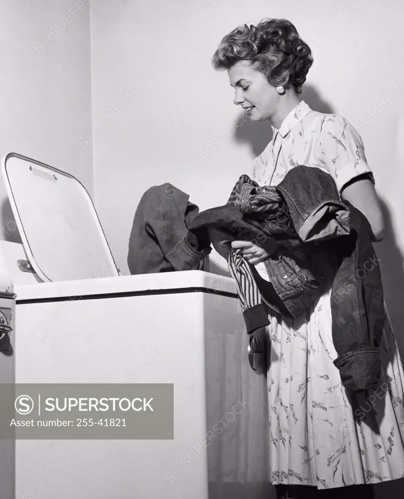 Side profile of a young woman putting clothes into a washing machine