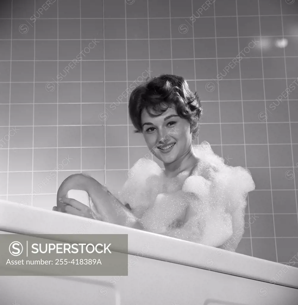 Portrait of young woman washing leg in bath