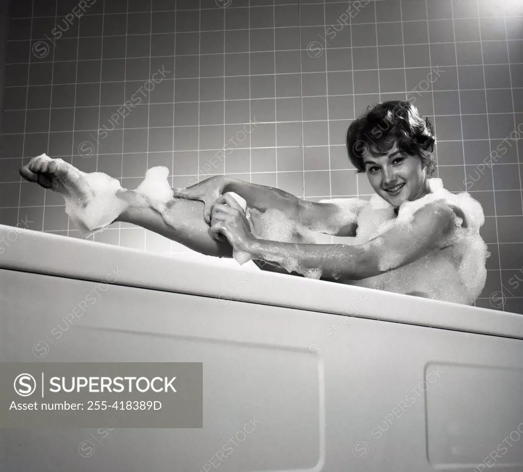 Portrait of young woman washing leg in bath
