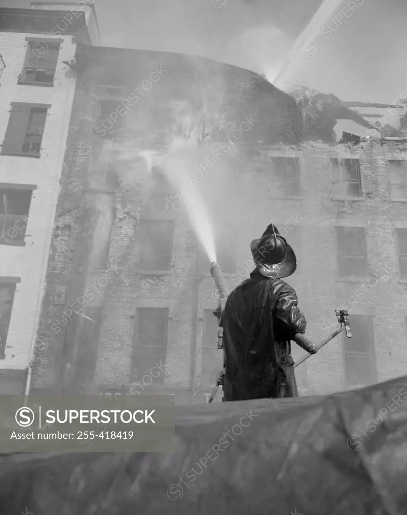 Firefighter pouring water on burning building, low angle view