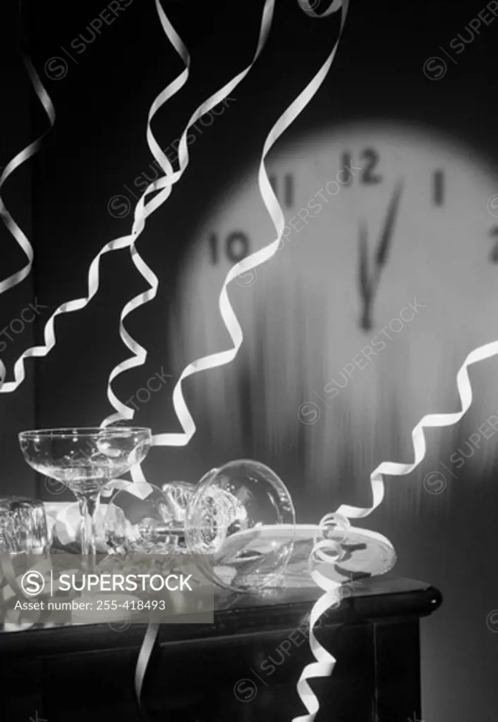 Empty champagne flutes with streamers and clock face showing five past midnight