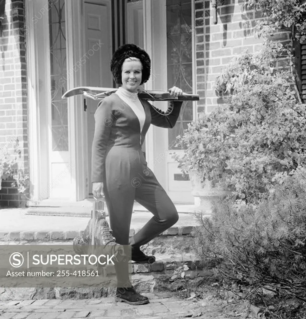 Young woman standing in front of house holding crossbow
