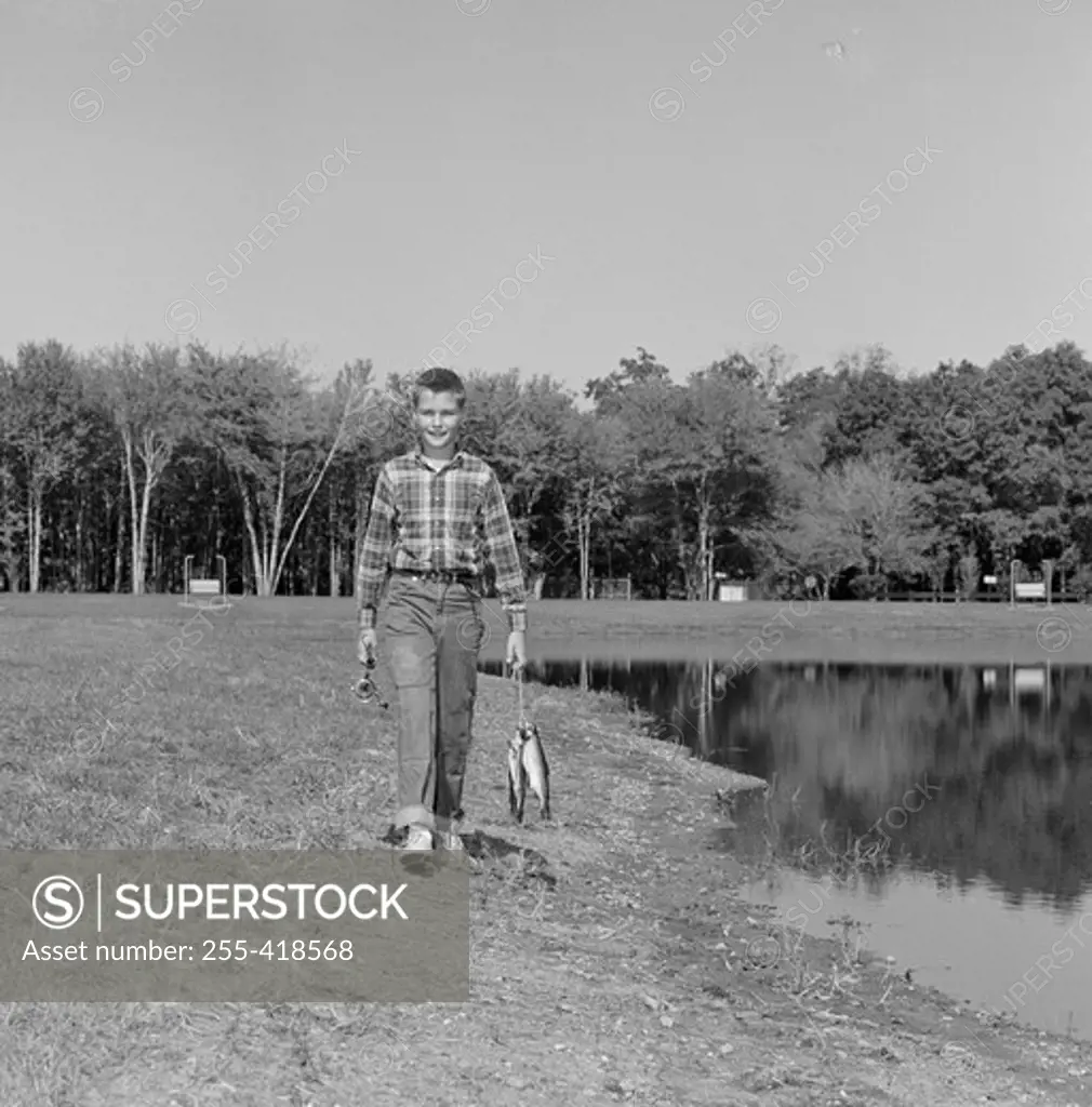 Boy walking along pond and carrying fish