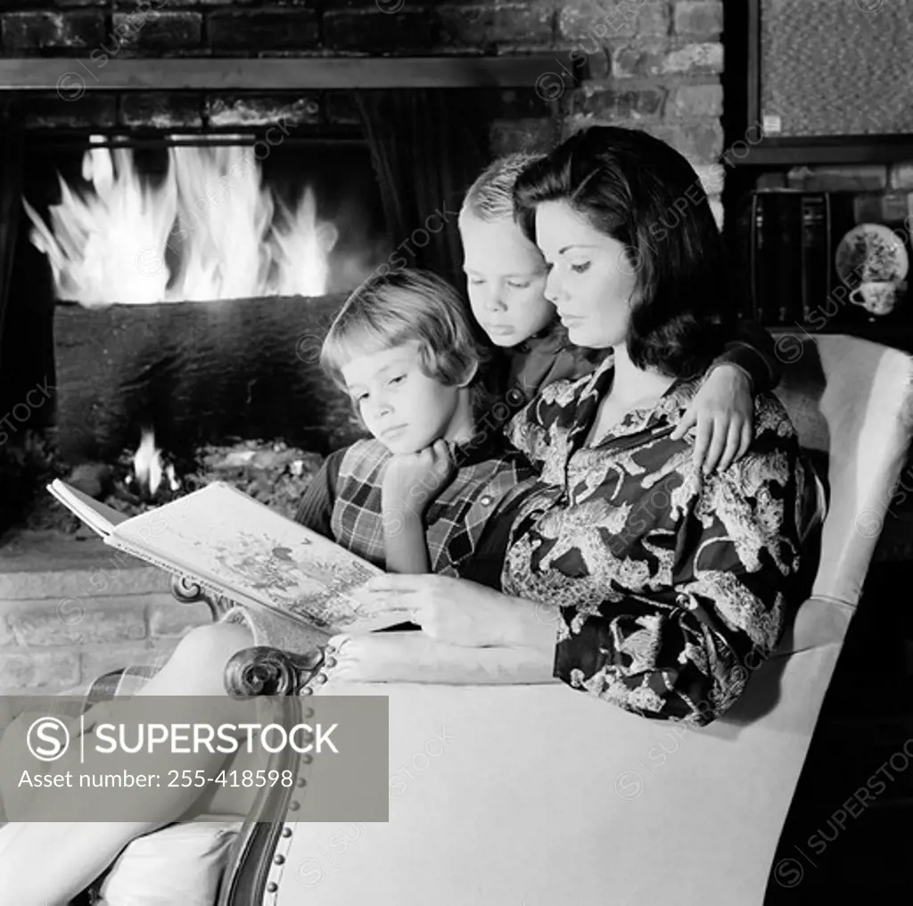 Mother, daughter and son reading book in living room