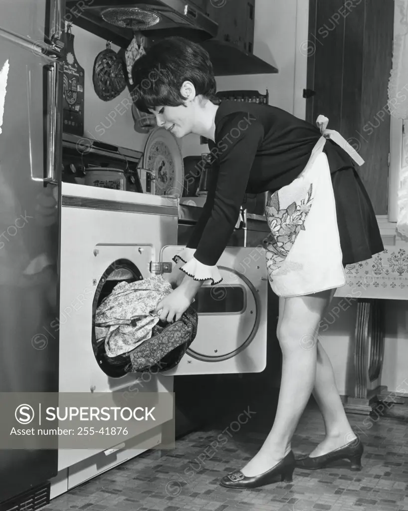 Side profile of a young woman putting clothes into a dryer