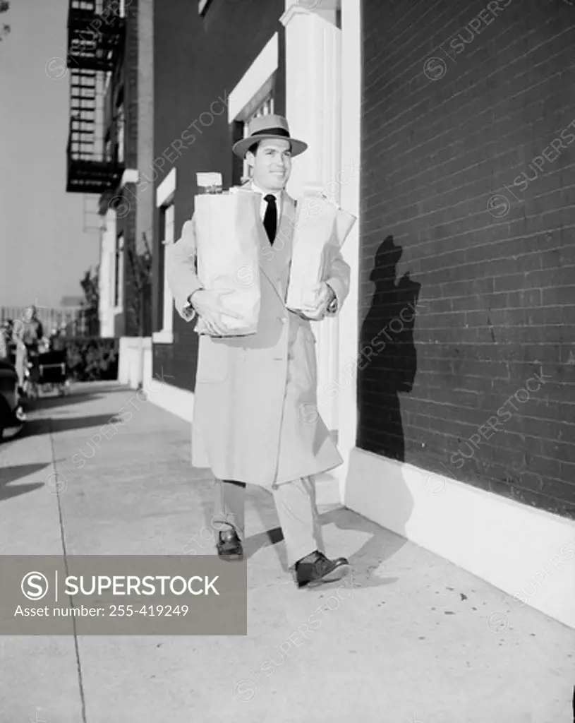 Young man walking on sidewalk carrying shopping bags
