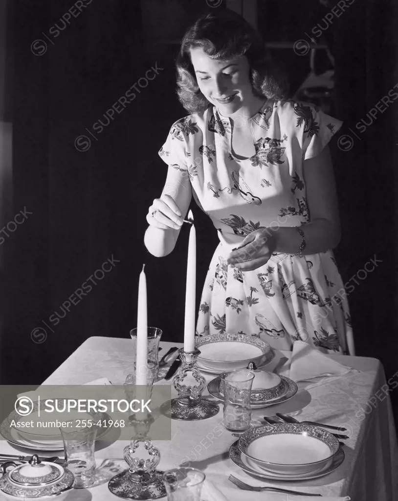 Young woman lighting a candle at a dining table