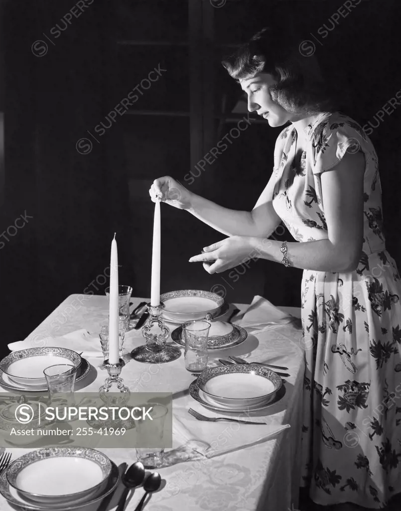 Side profile of a young woman lighting a candle at the dining table