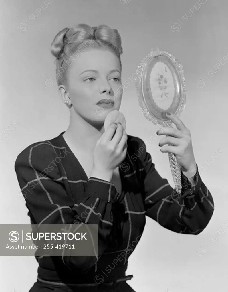 Portrait of woman looking at mirror and using powder puff