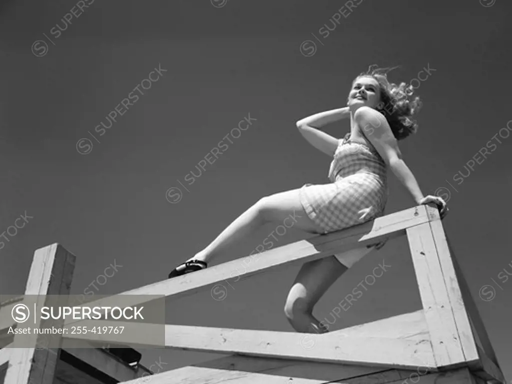 Low angle view of woman sitting on wooden fence