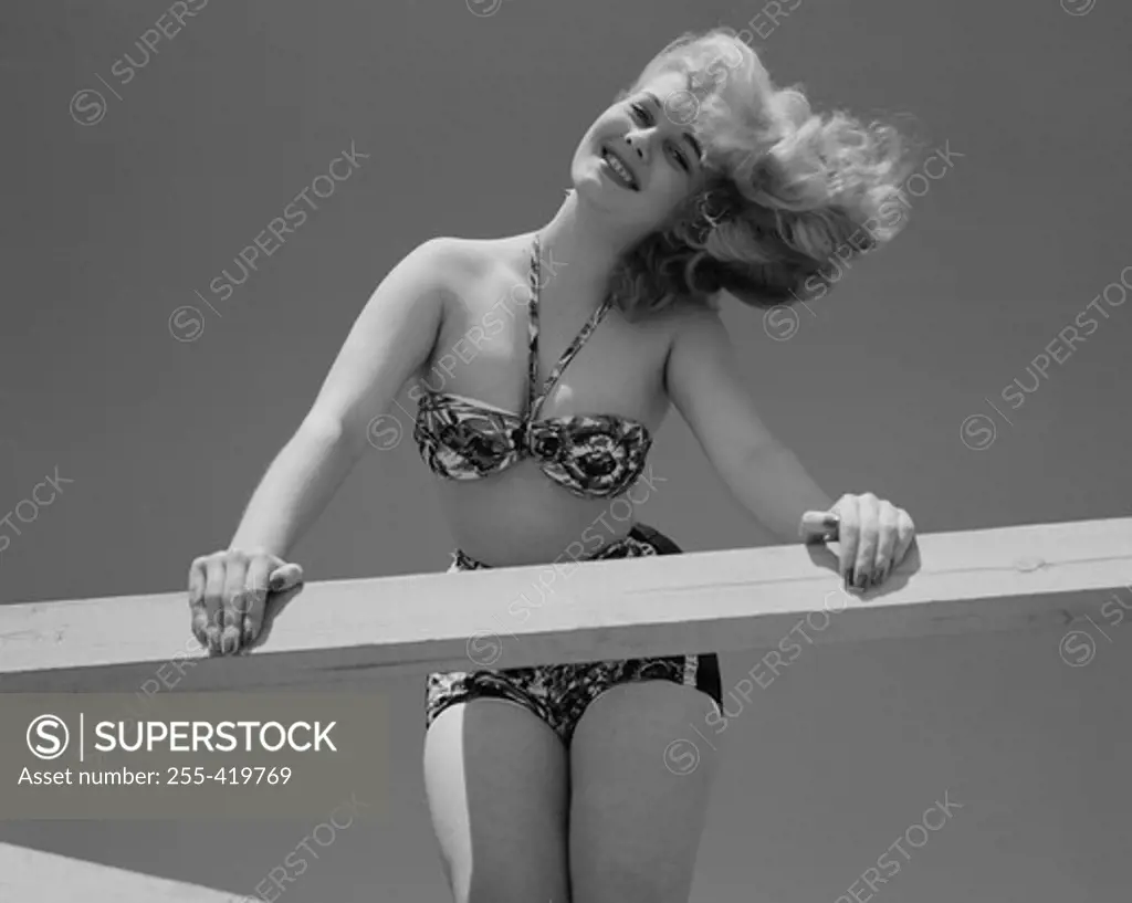 Low angle view of woman in bikini leaning on wooden fence