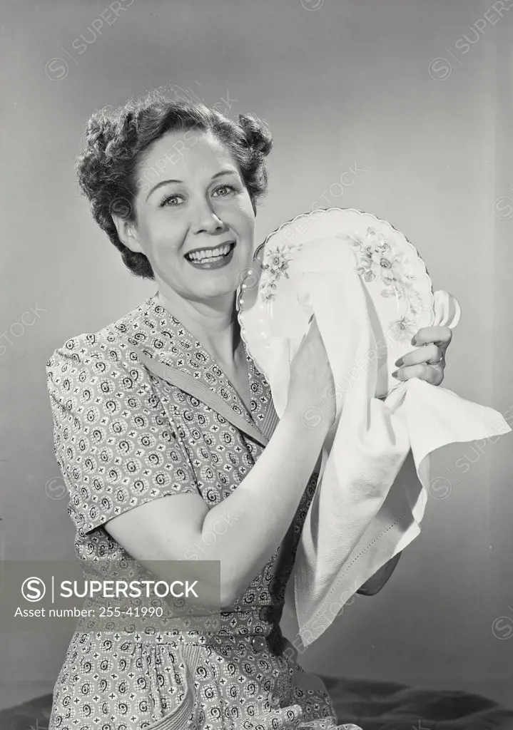 Vintage photograph. Brunette woman smiling in housedress holding up plate to dry