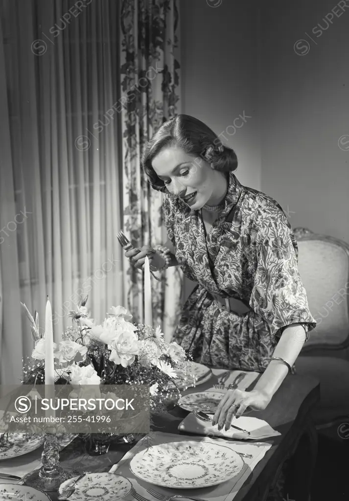 Woman placing silverware at dinner table.