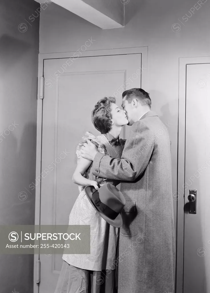Young couple kissing for goodbay in front of apartment door