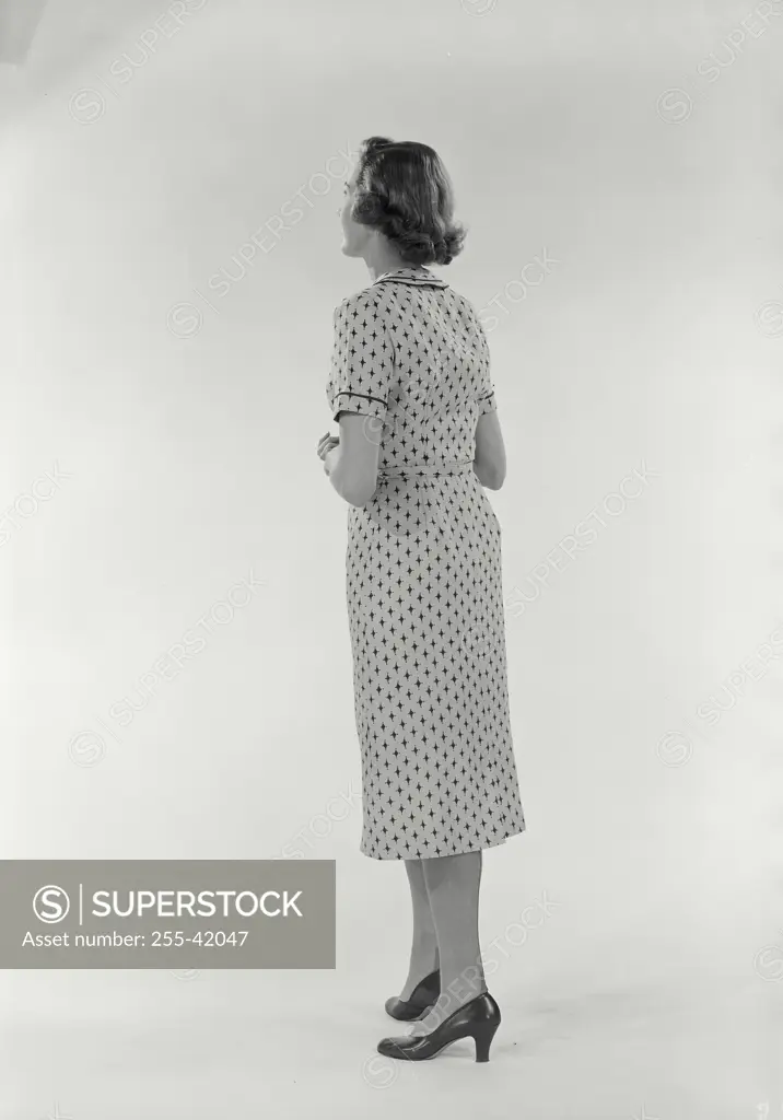 Vintage Photograph. Full length view from behind of woman standing on white background wearing diamond patterned dress, Frame 1
